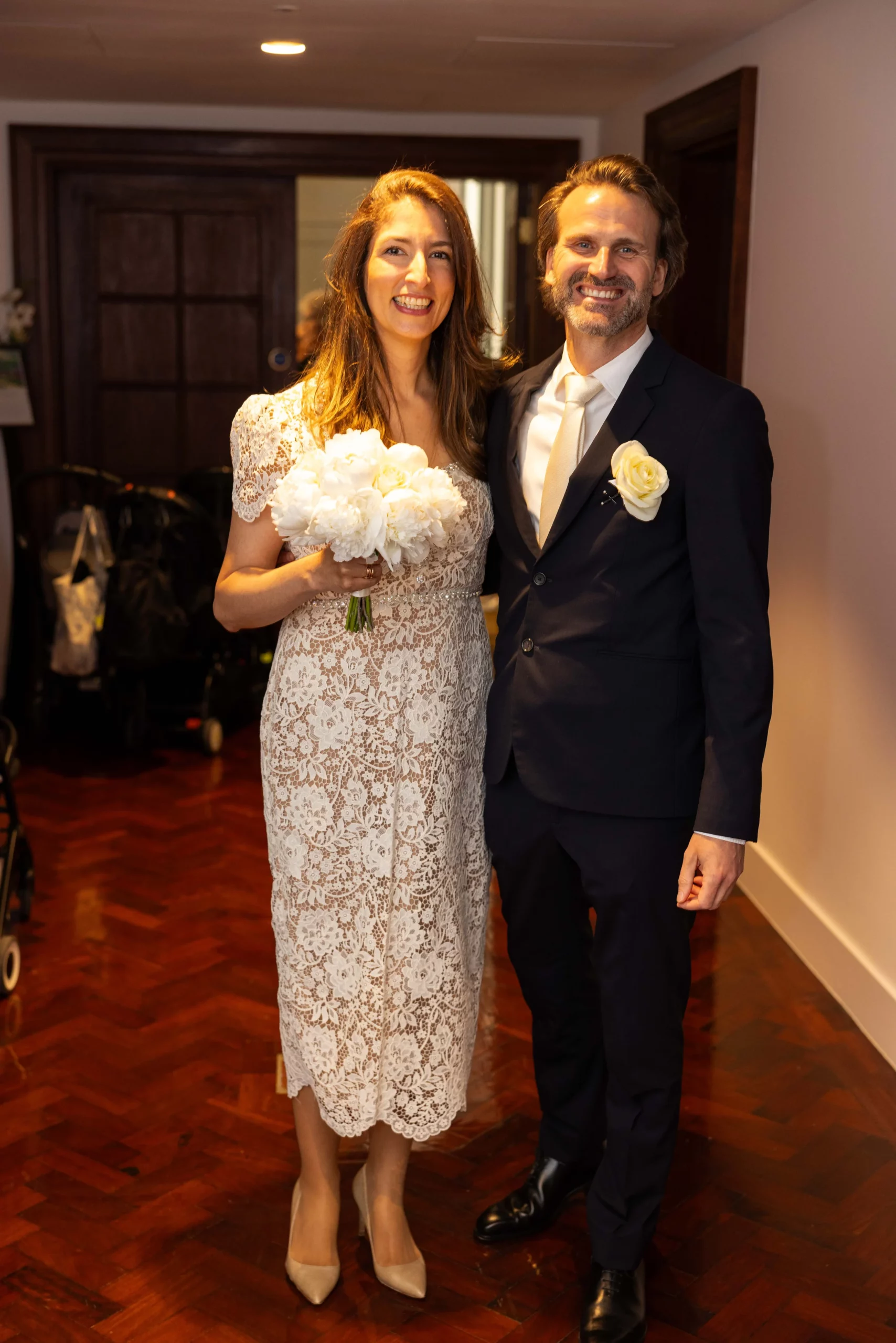 Bride and groom smiling with flowers indoors.